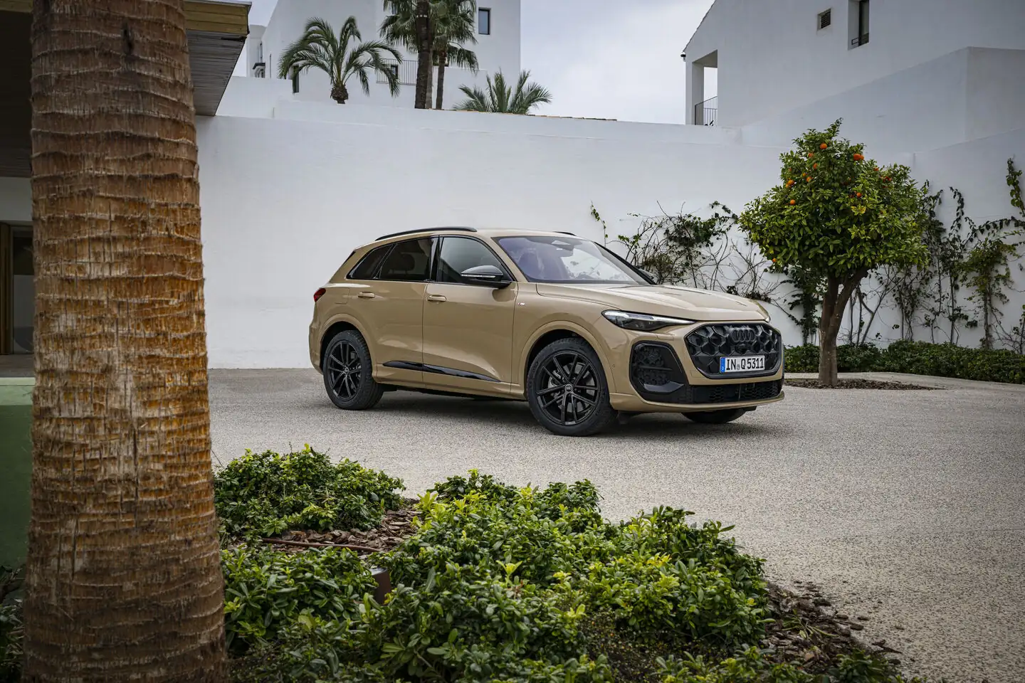 Audi Q5 třetí generace v barvě Sakhir Gold před budovou
