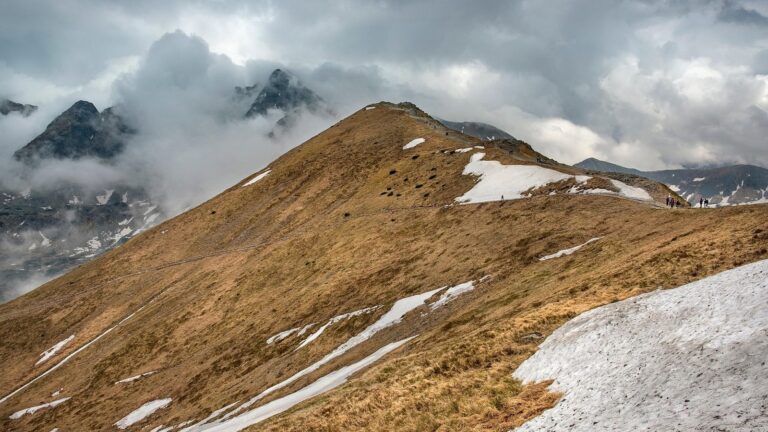 Travnatý horský hřeben se zbytky sněhu a mraky nad vrcholy