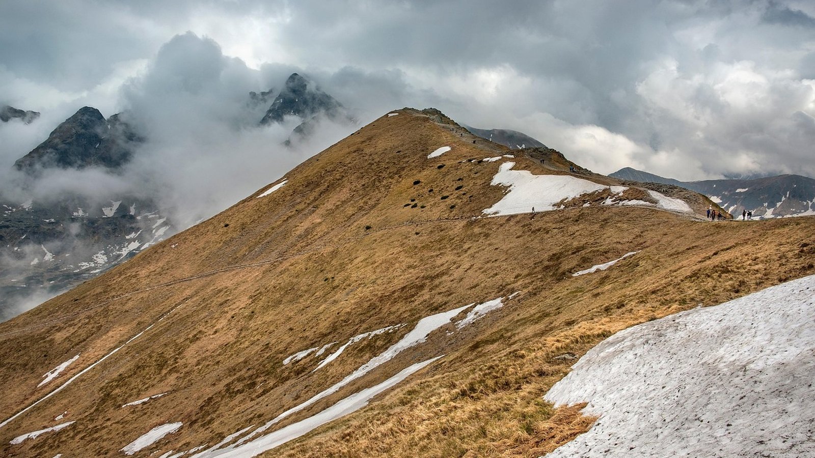 Travnatý horský hřeben se zbytky sněhu a mraky nad vrcholy